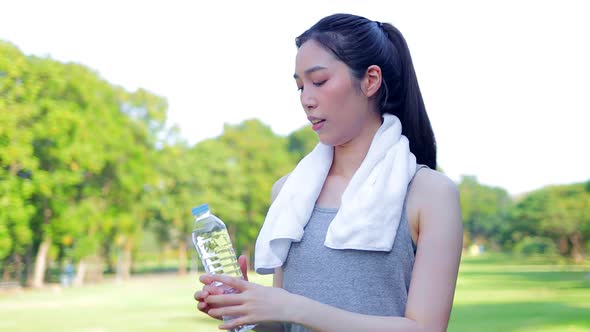 Beautiful Asian woman drinking water. She exercises in an outdoor park.