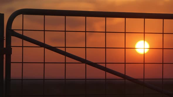 Close up silhouette of farm gate during beautiful sunset, static shot.