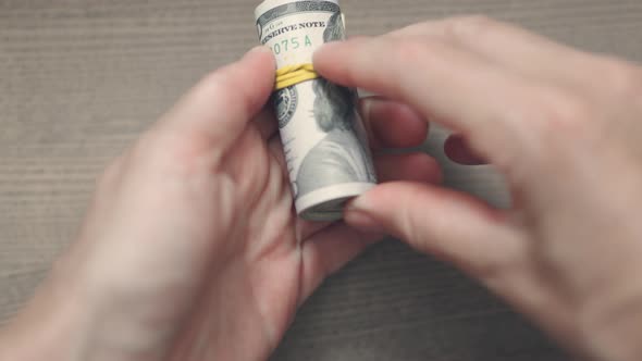 Hands Putting Yellow Rubber Band on a Roll of Hundred Dollar Bills