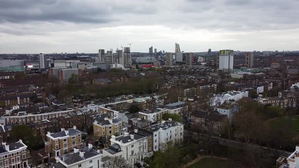 Aerial flyover rural suburb in London and skyline with skyscraper in background during cloudy day. N