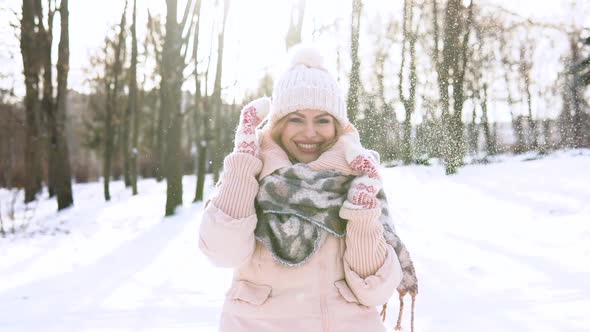 Young Woman in a Soft Pink Down Jacket White Hat Mittens and Scarf Smiling at the Camera