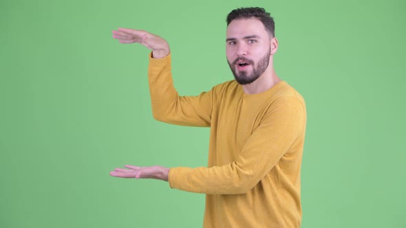 Happy Young Handsome Bearded Man Snapping Fingers and Showing Something