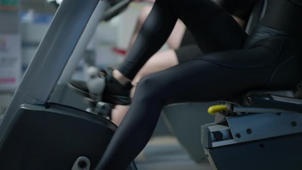 Side View Legs of Slim Women Riding Stationary Bike in Gym