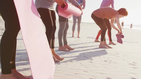 Multi-ethnic group of women folding sport mats on the beach and blue sky background