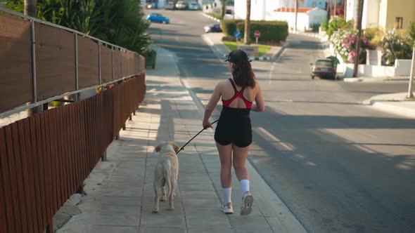 Back View Young Caucasian Fit Woman Walking with Dog on Cyprus Street Outdoors