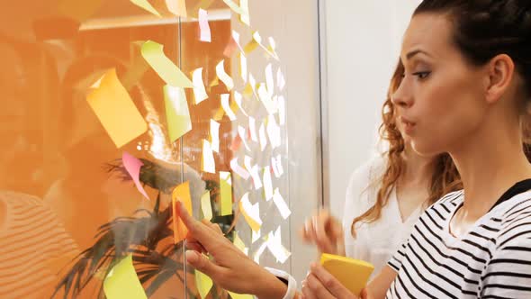 Female business executives interacting while reading sticky notes