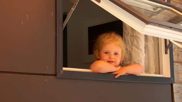 The Cute Little Girl Looks Out of the Open Window