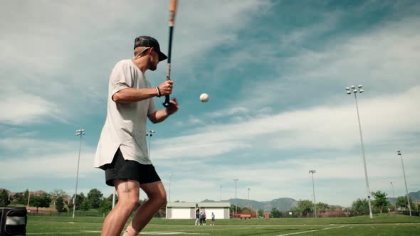 A low wide shot of a professional male baseball player practices tossing a ball into the air and hit