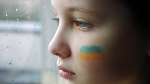 girl child at the window with the flag of ukraine on a cheek. State support in war. United Europe ag