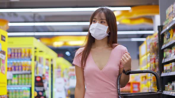 Asian beautiful woman wearing face mask and holding shopping basket in supermarket department store.