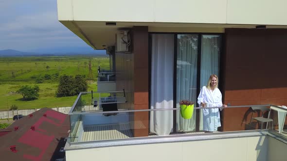 Drone view of woman in white coat with cup of coffee, on hotel balcony
