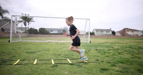 A young athlete practices fast feet over a speed ladder at the park as part of her running warmup.