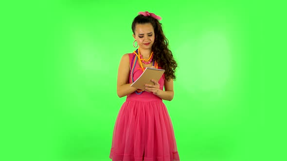 Girl Stands and Thinks, Then Happy Writes with Pencil in Notebook. Green Screen