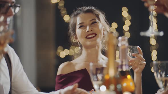 Close-up Portrait of Asian Girl Raising Glass of Champagne and Clinking Glasses with Everyone at