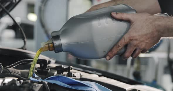 Mechanic Hands. Engine Oil Flows From The Canister Into The Engine Of A Car.