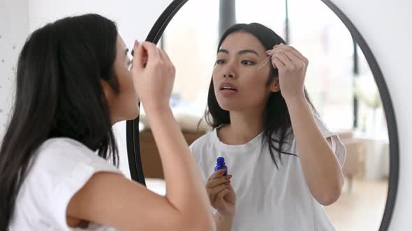 Asian Pretty Girl in White Tshirt Stands in Front of a Mirror at Home Does Her Morning Beauty