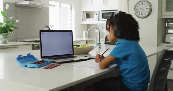 Happy biracial boy sitting at table using laptop with copy space and having online classes