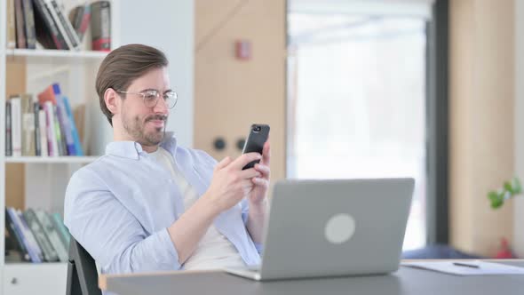 Man in Glasses with Laptop Using Smartphone in Office