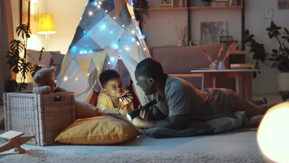 Afro-American Father Reading Fairytale to Child in Cozy Dark Room