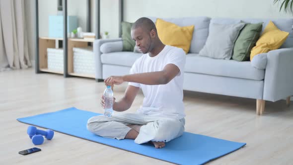 Young African Man Drinking Water on Yoga Mat at Home