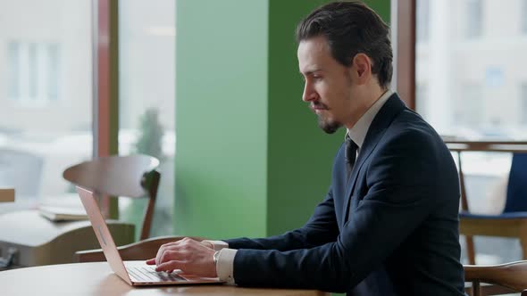 Side View of Concentrated Caucasian Man with Mustache Typing on Laptop Keyboard Messaging Online