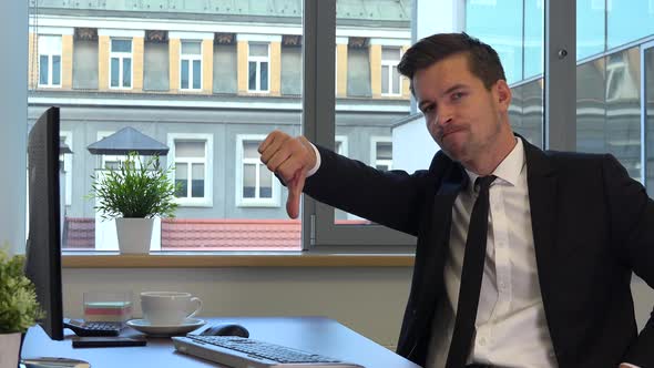 An office worker in a suit works on a computer, gets upset and shows a thumb down to the camera