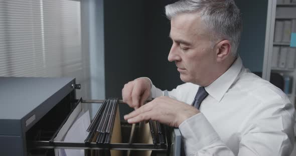 Corporate businessman searching for files in the filing cabinet