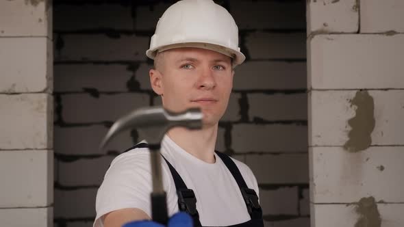 Portrait of a Construction Worker in a White Helmet with a Hammer in His Hands