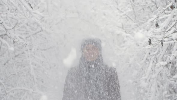 An Adult Man Stands Under Snowcovered Branches From Which Snow Falls in Slow Motion