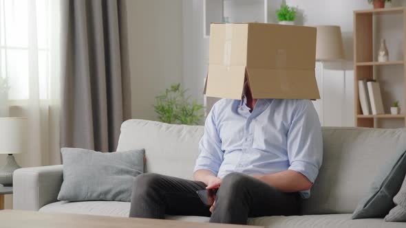 Man Holds Smartphone While Sit on Sofa with Box on His Head Using Parcel Tracking Application Leave