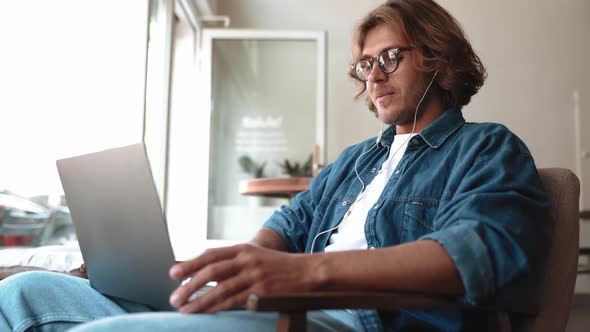 Positive blond man in eyeglasses talking by video call on laptop