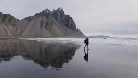Man With Backpack Walking Along Wet Beach Towards Sea By Vestrahorn