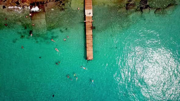 Overhead jib up view of people snorkeling at Grandi Beach with fishing boats on shore, Dutch island