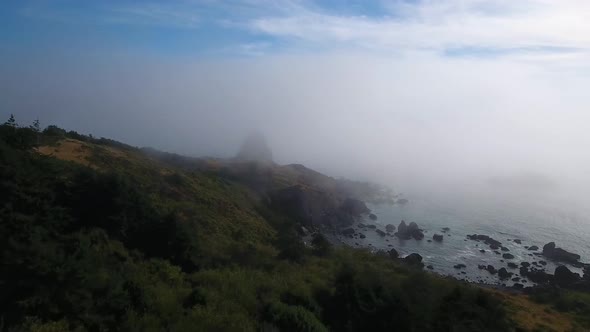 AERIAL: Drone shot pushing towards a mysterious rock formation shrouded by fog.