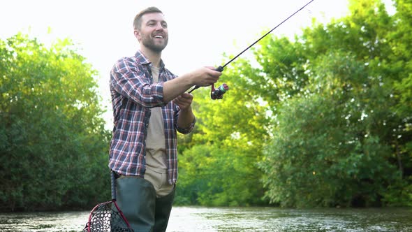 A Fisherman Throws a Fishing Rod Standing Kneedeep in the Water of the River