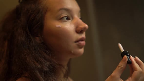 Brunette Young Woman with Curly Hair Applies Makeup Base