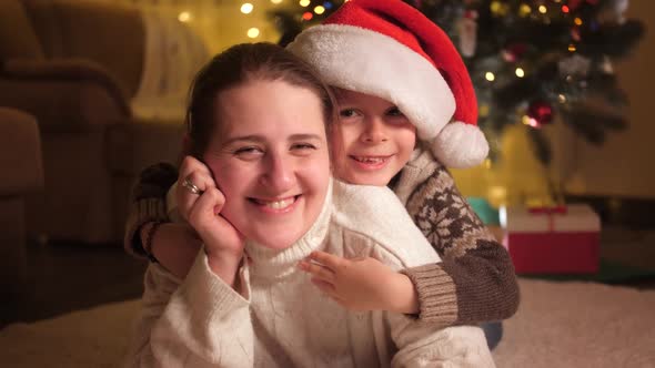 Portrait of Smiling Mother with Son in Santa Hat Lying on Floor on Christmas Eve