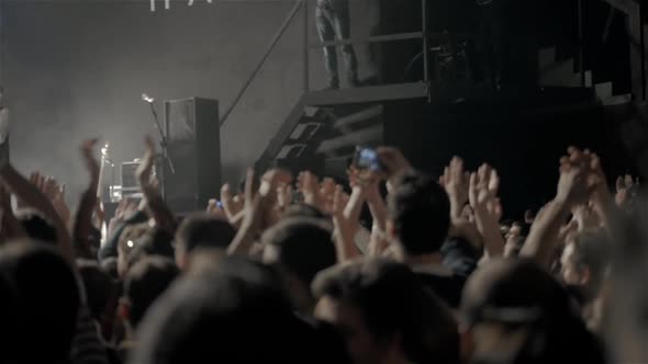 Audience with Hands Raised at a Music Festival and Lights Streaming Down From Above the Stage