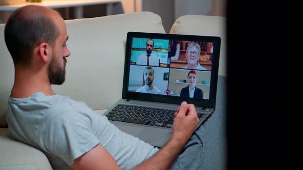 Over Shoulder View of Man in Pajamas Having Online Conversation with Teammates