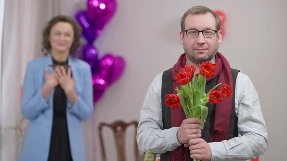 Portrait of Adult Caucasian Stylish Man in Eyeglasses Posing with Bouquet of Flowers Indoors with