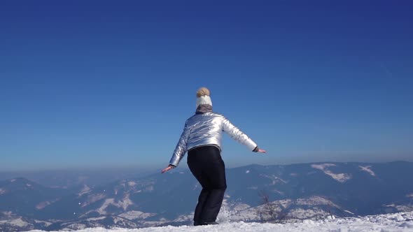 Young Woman Is Jumping at the Top of Mountain with Beautiful View Powerful Snowy Mountains and Blue