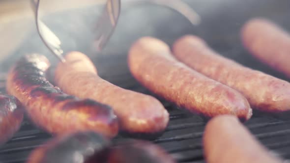 Slow Motion of Tongs Flipping Sizzling Gristly Sausage on Fiery and Smokey BBQ Grill