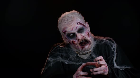 Sinister Man with Horrible Scary Halloween Zombie Makeup in Convulsions Making Faces Trying to Scare