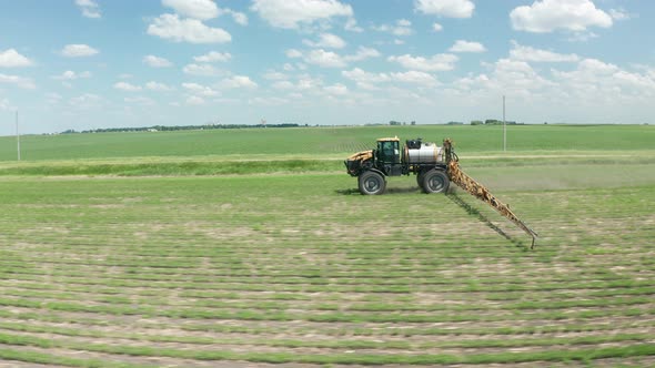 Aerial, farm tractor spraying pesticides on crops. Hot summer blue sky day. Series