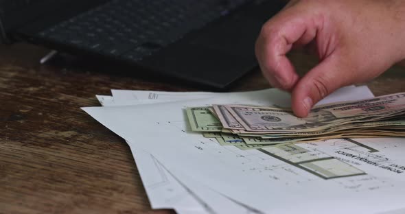 Self Employed Businessman Counts Cash Income Holding Dollar Banknotes Sitting at Table with Laptop