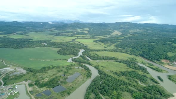 Aerial Drone View Beautiful Natural Scenery of Green Meadow with River Mountains in Background