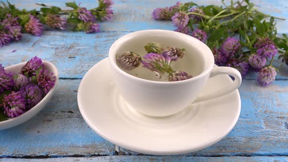 Brewing a tisanes from red clover in a white cup. Composition on vintage light blue wooden tabletop 