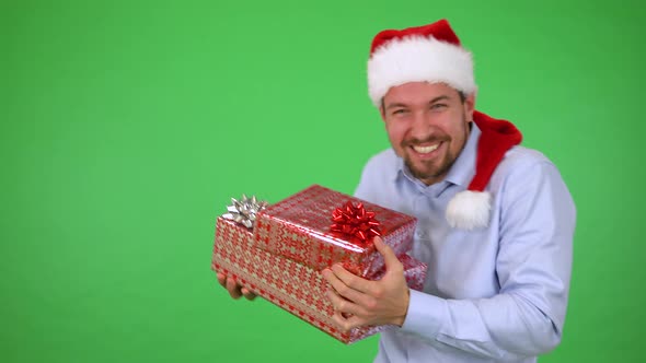 A Man in a Christmas Hat Holding a Present Dances and Smiles at the Camera - Green Screen Studio