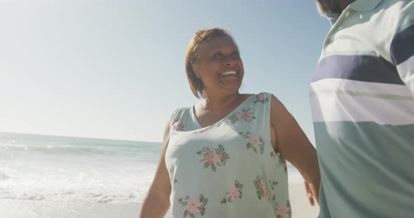 Smiling senior african american couple embracing and walking on sunny beach