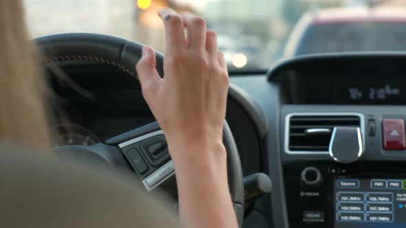 Rear view of female driver behind steering wheel driving a car on a city street.